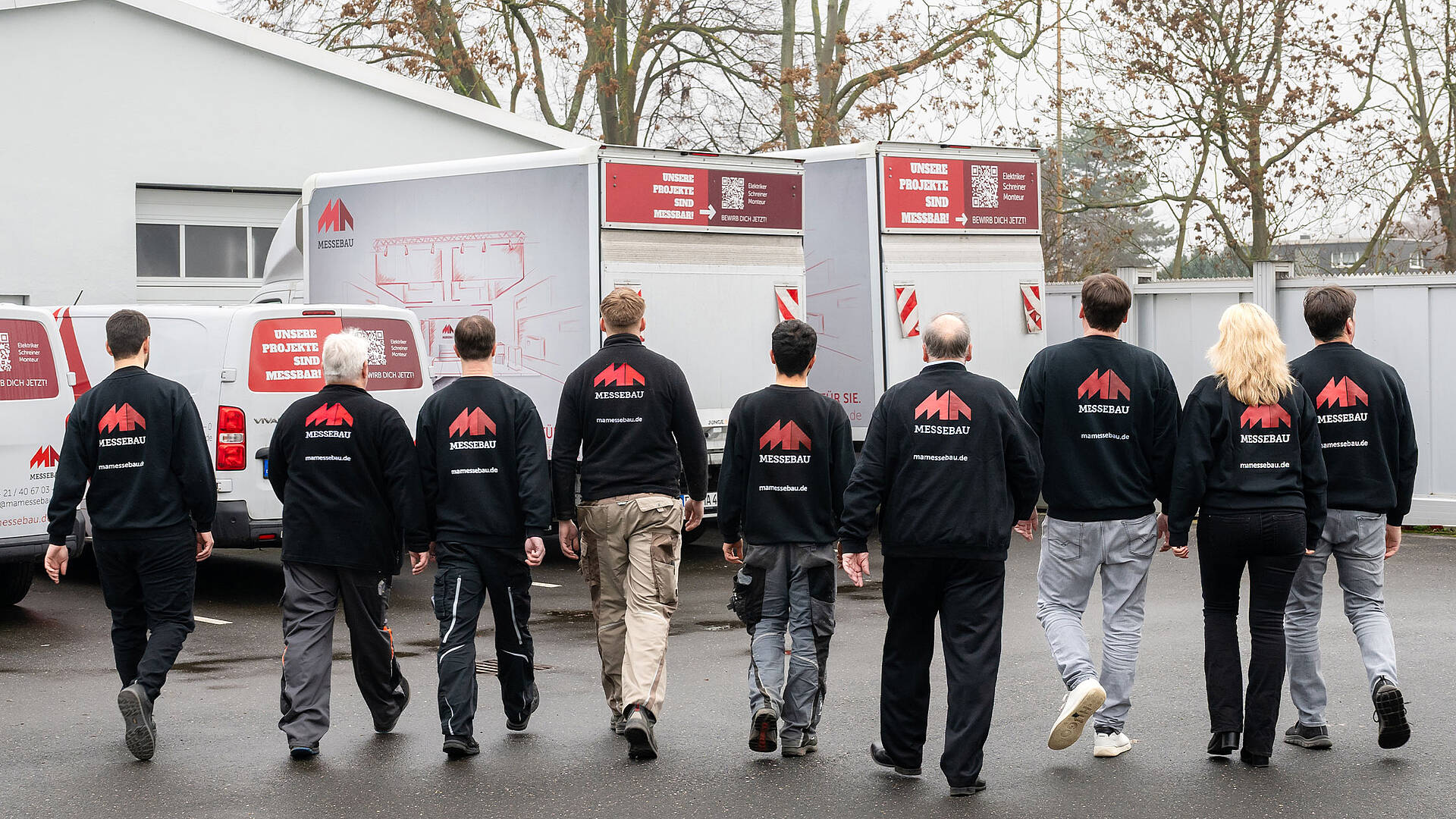 MA Messebau Header Events Mitarbeiterreihe von hinten die auf Fahrzeuge zulaufen