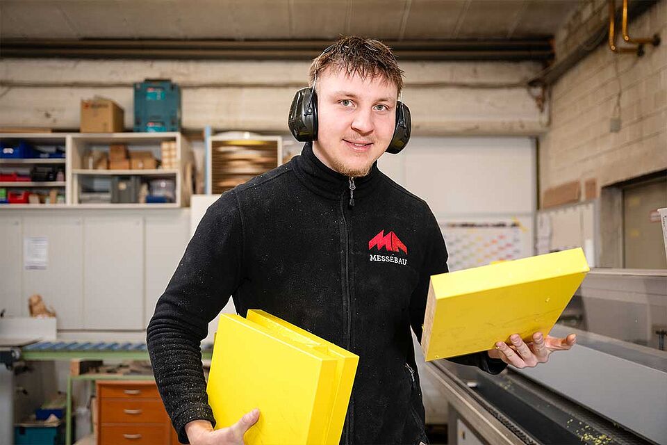MA Messebau Mitarbeiter Fertigung mit gelben Kunststoffplatten in der Hand